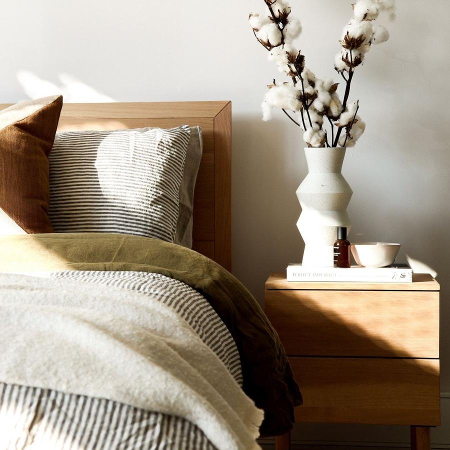 swath of sunlight shines across a well made bed and bedside table with a vase of cotton plants